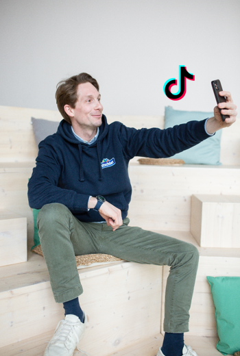 Philip Hitschler Becker hält sein Smartphone hoch und macht ein Selfie mit dem Icon von TikTok